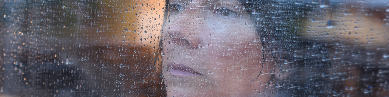 moody image of woman's face looking out rainy window